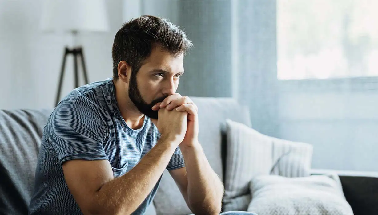 Ein Mann sitzt auf dem Sofa und überlegt