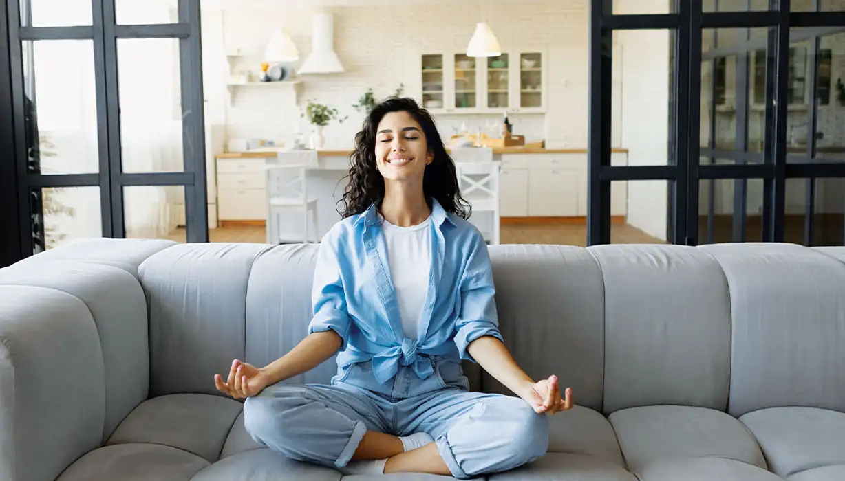 Junge Frau meditiert lächelnd auf dem Sofa
